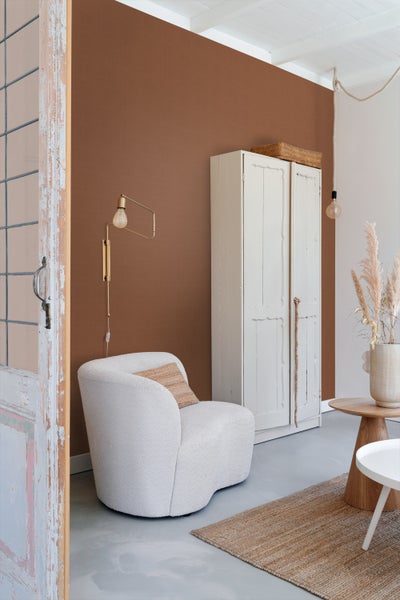 Wohnzimmer mit Sessel, Schrank und Beistelltischen auf einem Teppich