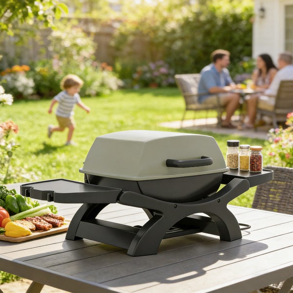 Moderner tragbarer Tischgrill auf Gartentisch in hellem Garten mit Familie im Hintergrund. Grill mit Seitenablagen für Gewürze und Fleisch.