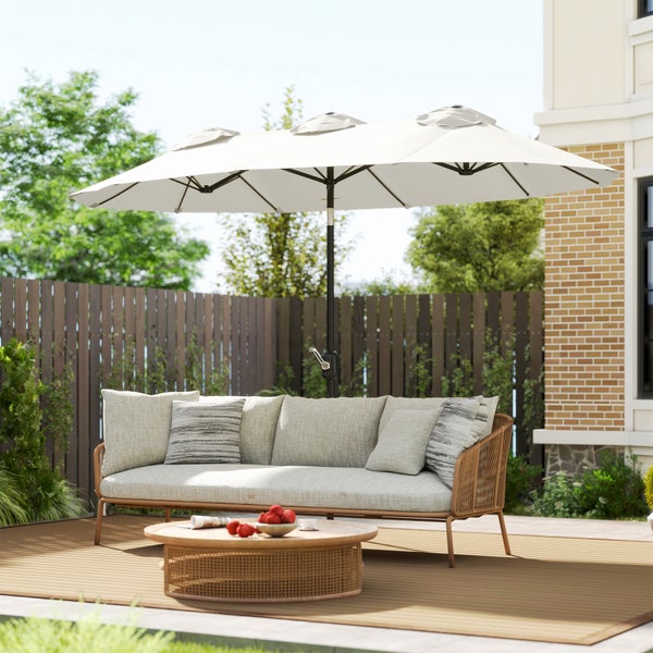 Modernes Garten-Set mit grauem Sofa, rundem Couchtisch aus Geflecht und großem weißem Sonnenschirm auf einer Terrasse mit Holzzaun.