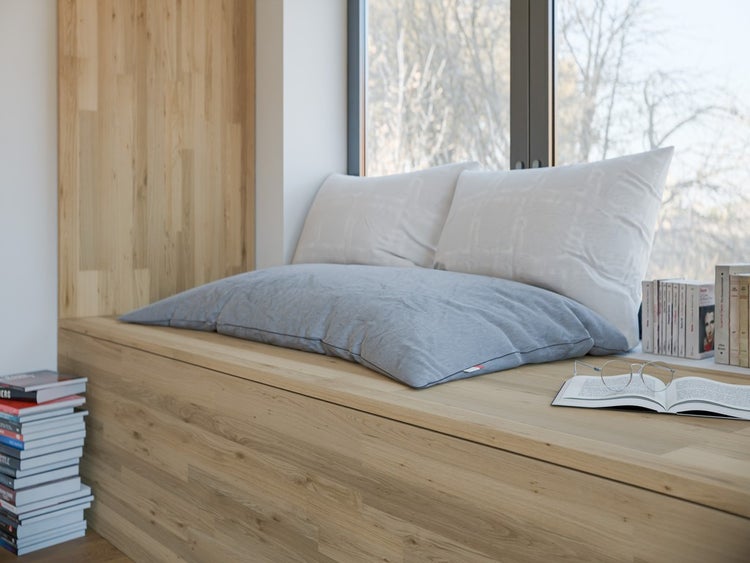 Ein heller und organisierter Leseplatz mit einer eingebauten Holzbank und Wandverkleidung aus hellen Holzpaneelen, Kissen und Büchern an einem Fenster.