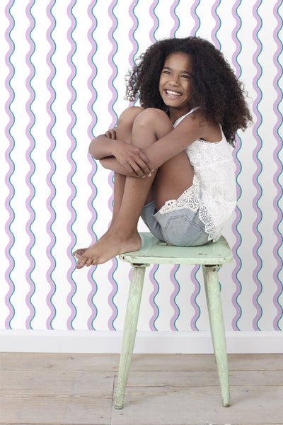 Mädchen sitzt auf einem Hocker vor einer Wand mit Wellentapete