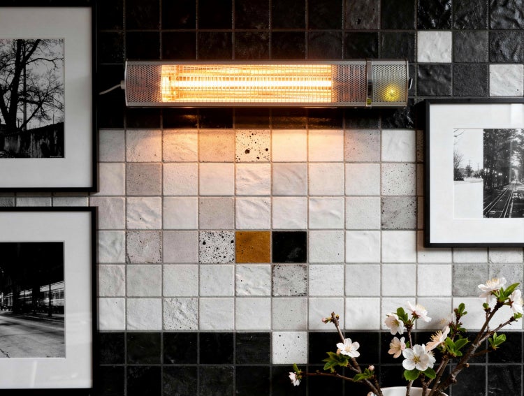 An der Wand montierter Heizstrahler in einem Raum mit Dekorfliesen und gerahmten Bildern