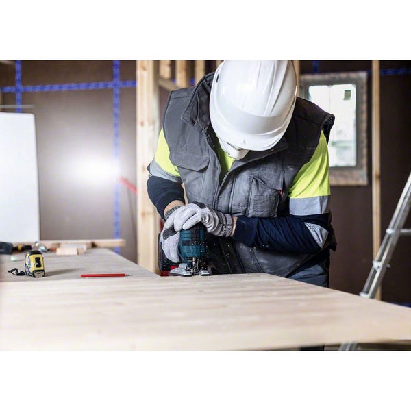 Ein Bauarbeiter mit Helm und Handschuhen bearbeitet ein Holzbrett mit einer Oberfräse in einer hellen, organisierten Baustelle.