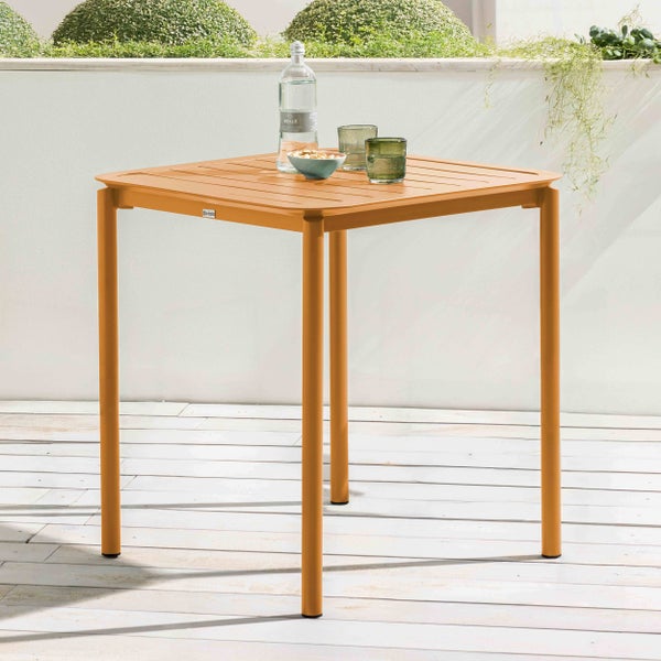 Quadratischer Gartentisch aus Metall mit Lattenoberfläche auf einer hellen Terrasse mit einer Wasserflasche und Gläsern.