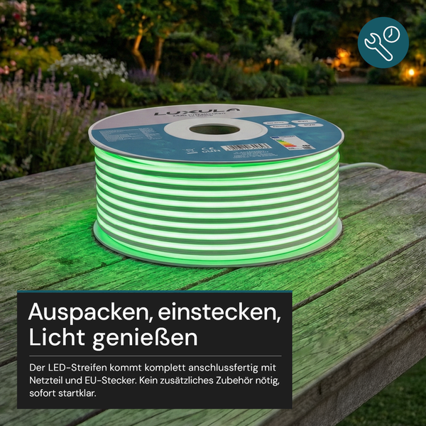 Aufgerollter grün leuchtender LED-Streifen auf einem Holztisch im Garten, anschlussfertig mit Netzteil für eine einfache Montage.