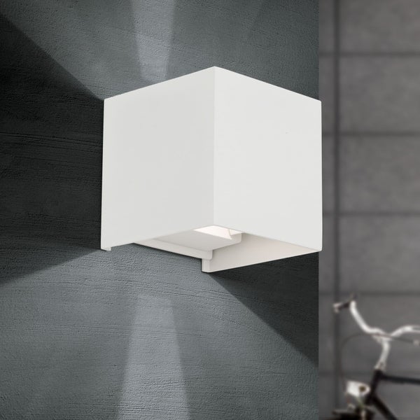 Würfelförmige Wandleuchte mit Lichtaustritt nach oben und unten an einer strukturierten Wand.