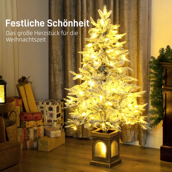 Verschneiter künstlicher Weihnachtsbaum mit warmweißen LED-Lichtern in einem beleuchteten Sockel, umgeben von Weihnachtsgeschenken.