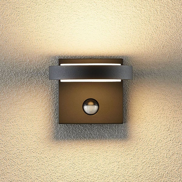 Quadratische Außenwandleuchte in Anthrazit mit integriertem Bewegungsmelder und warmweißem Lichtschein nach oben und unten an einer Wand.
