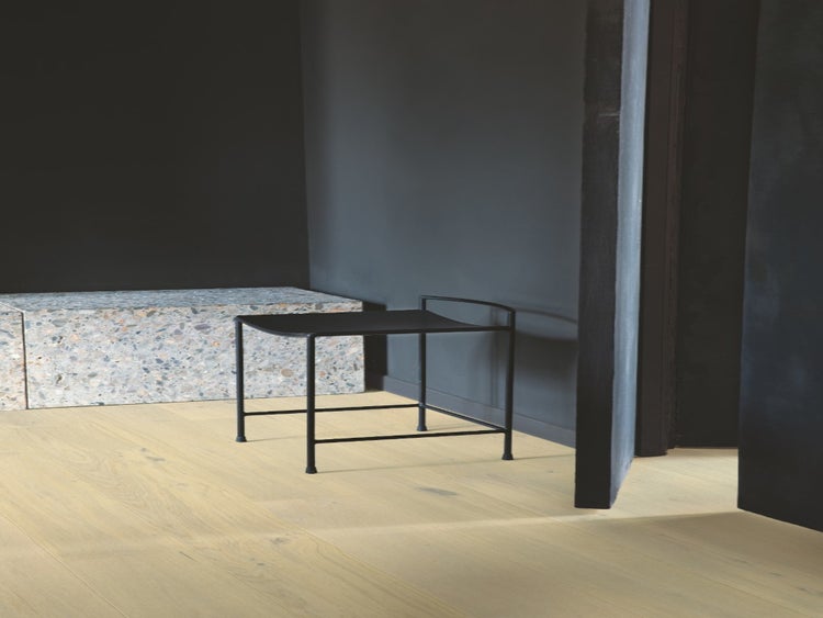 Hellbrauner Holzfußboden in einem minimalistischen Raum mit dunklen Wänden, einem schwarzen Metallbeistelltisch und einem Steinelement.