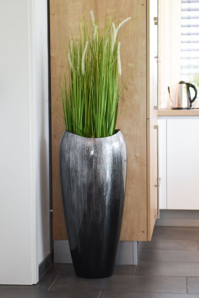 Hohe Bodenvase in Dunkelgrau mit gebürsteter Optik und künstlichem Ziergras vor einem hellen Holzschrank in einer modernen Küche.