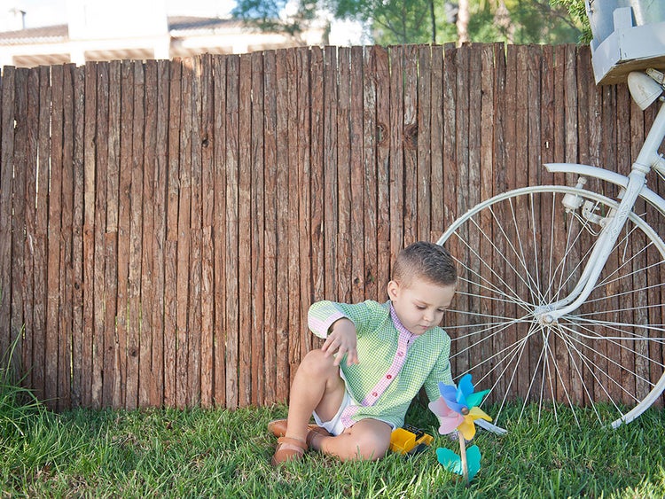 Junge spielt mit Windrad vor Holzzaun und Fahrrad