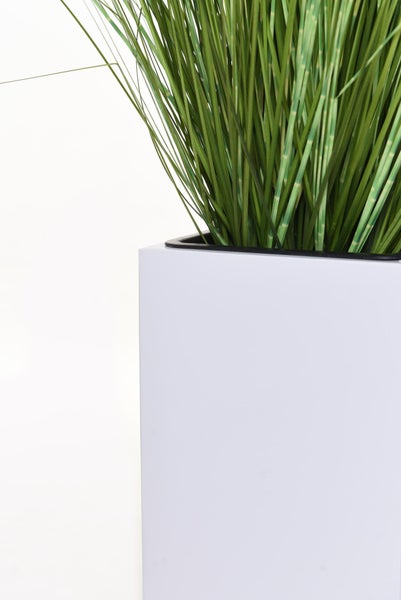 Künstliches Zebragras mit gestreiften Halmen in einem quadratischen weißen Pflanzgefäß.