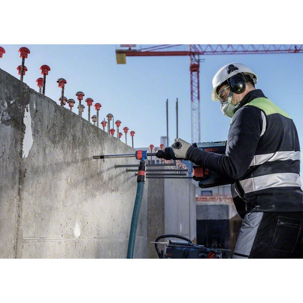Ein Bauarbeiter bohrt mit einer Bohrmaschine ein Loch in eine Betonwand auf einer Baustelle.