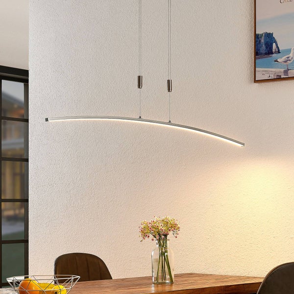 Moderne, gebogene LED-Pendelleuchte aus Metall über einem Holzesstisch in einem hellen Raum.