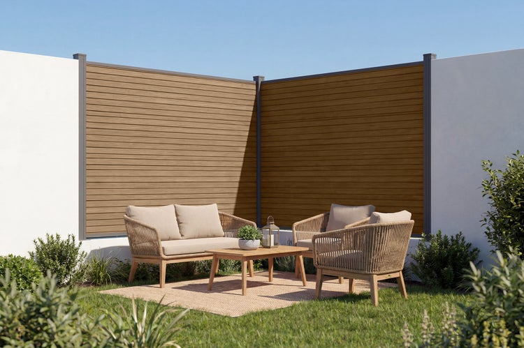 Moderne Gartensitzecke mit Lounge Möbeln aus Geflecht vor einem Sichtschutzzaun aus Holzoptik Elementen im Außenbereich.