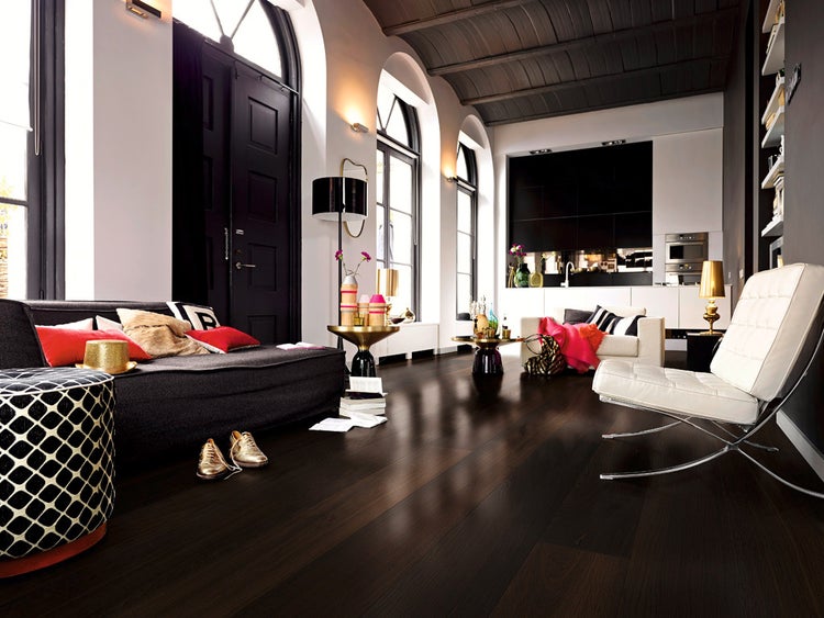 Moderner Wohnraum mit dunklem Boden, schwarzem Sofa, weißem Designersessel, Rundbogenfenstern und offener schwarz-weißer Küche.