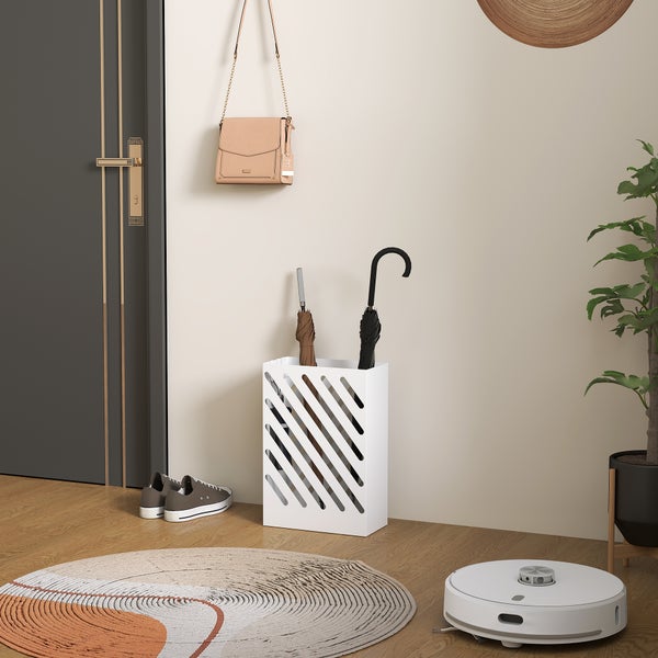 Moderner Schirmständer aus Metall mit diagonalen Schlitzen in einem hellen Flur mit Holzboden, Schuhen und einer Handtasche an der Wand.