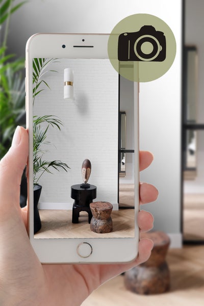 Hand hält Smartphone, das ein Interieur mit Pflanze, Dekoration und Möbeln zeigt