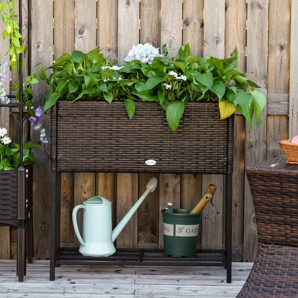 Hochbeet aus Polyrattan mit Ablageregal und Pflanzen wird mit einer Sprühflasche gegossen.