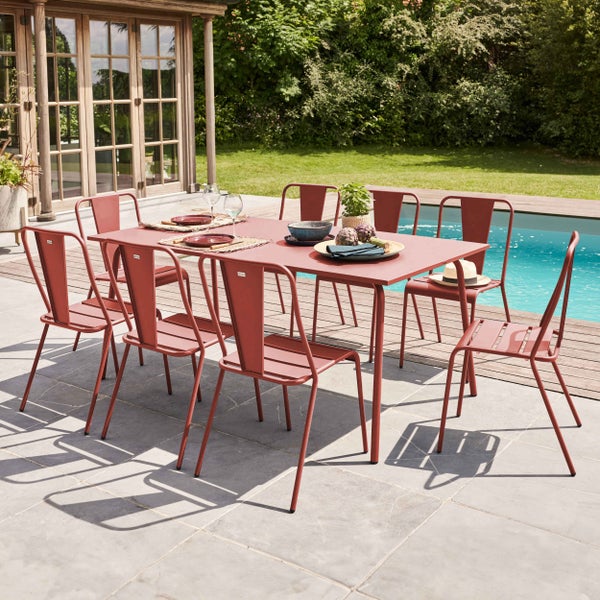 Modernes Gartenmöbel-Set mit rechteckigem Metalltisch und acht Metallstühlen auf einer hellen Steinterrasse neben einem Pool und einem Gartenhaus.