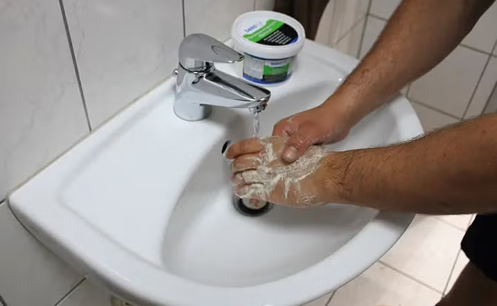 Person wäscht sich die Hände mit Handwaschpaste in einem Waschbecken.