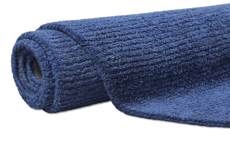 Badeteppich in Blau mit geschwungener Kante und geometrischem Muster sowie Detailansicht der weichen Faserstruktur.