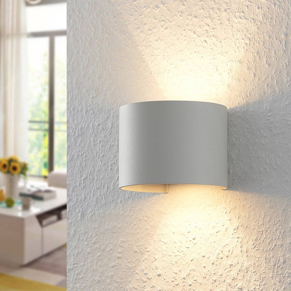 Moderne Wandleuchte mit Lichtaustritt nach oben und unten an einer strukturierten weißen Wand in einem hellen Wohnraum.