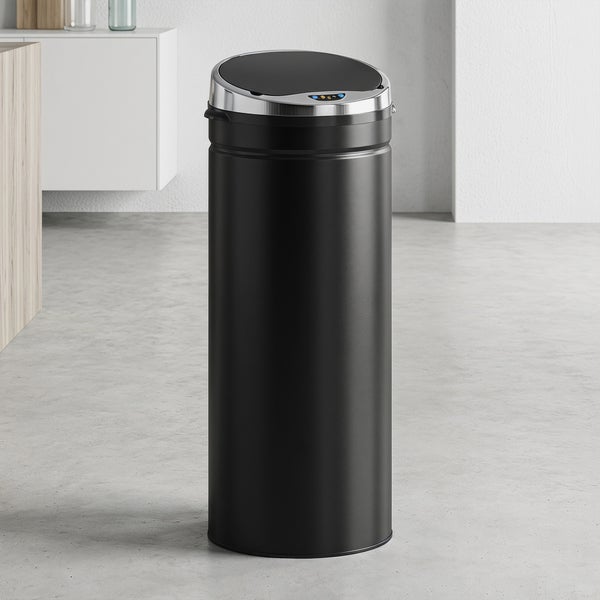 Zylindrischer Sensor-Mülleimer aus schwarzem Metall mit Chromdeckel in einem modernen Raum mit Betonboden und weißem Schrank.