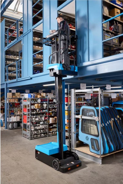 Person auf einem HanseLifter Elektro-Kommissionierer erreicht hohe Regale in einem organisierten Lager mit blauen Metallregalen.