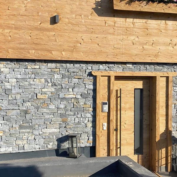 Hauseingangsbereich mit Natursteinmauerwerk aus Schiefer und einer rustikalen Holztür mit Glaseinsatz und Vordach.
