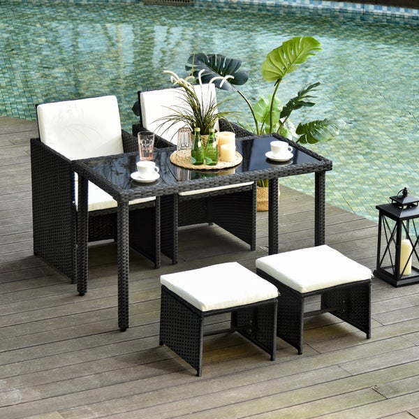 Gartenmöbel-Set aus Polyrattan bestehend aus Tisch mit Glasplatte, zwei Sesseln und zwei Hockern mit weißen Sitzkissen auf Holzterrasse am Pool.