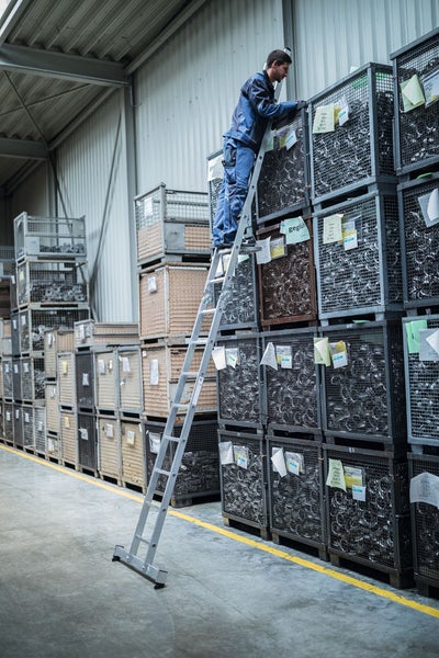 Mann auf einer Leiter vor Gitterboxen in einer Lagerhalle