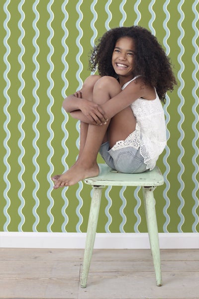 Mädchen sitzt auf einem Hocker vor einer gemusterten Tapete