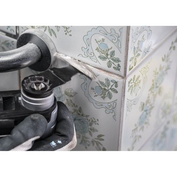 Eine Person mit Arbeitshandschuhen entfernt Fugen mit einem Multifunktionswerkzeug von den Fliesen.