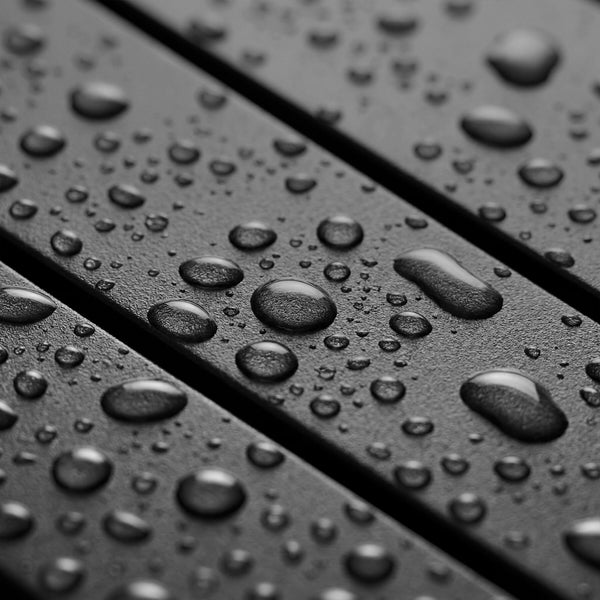 Nahaufnahme von Wassertropfen auf einer strukturierten, wasserabweisenden Oberfläche mit parallelen Lamellen.