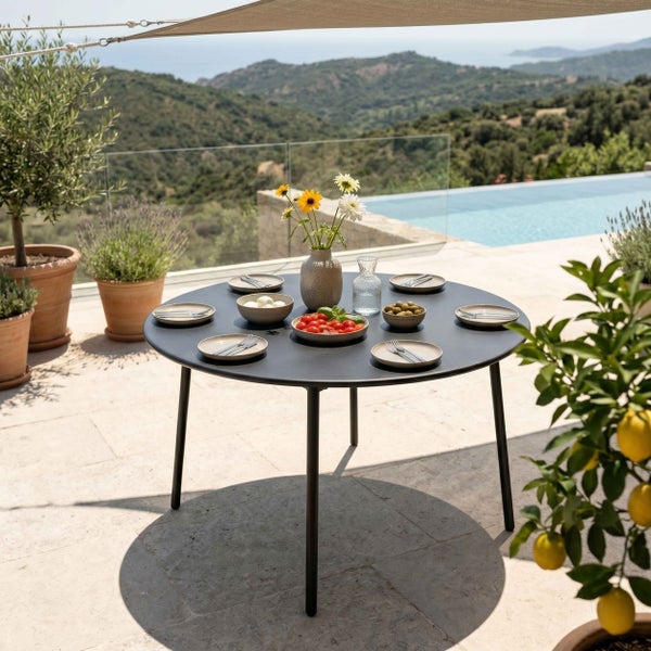 Runder Gartentisch aus Metall auf einer Terrasse mit gedecktem Tisch, im Hintergrund ein Pool und eine Hügellandschaft.
