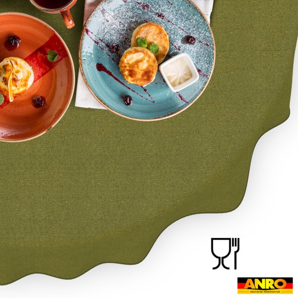 Strukturierte Tischdecke mit Wellenrand auf einem gedeckten Tisch mit Tellern. Lebensmittelecht-Symbol und ANRO Deutsche Manufaktur Logo.