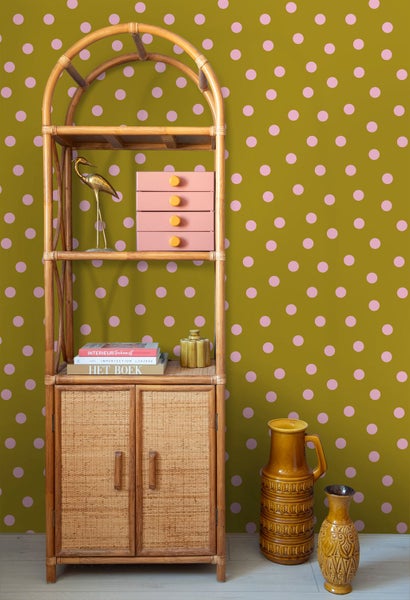 Vliestapete mit Punktmuster in Rosa auf Ocker, kombiniert mit einem Bambusregal und Keramikvasen im Retro-Stil.