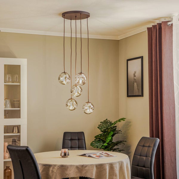 Fünfflammige Pendelleuchte mit Glasschirmen über einem runden Esstisch mit gepolsterten Stühlen in einem hellen, modern eingerichteten Esszimmer.