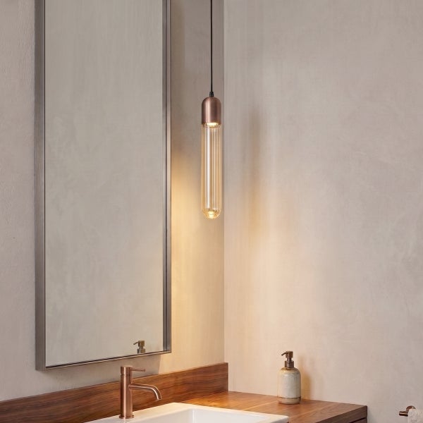 Moderne Pendelleuchte mit geriffeltem Glaszylinder neben einem Badezimmerspiegel und Waschtisch aus Holz.