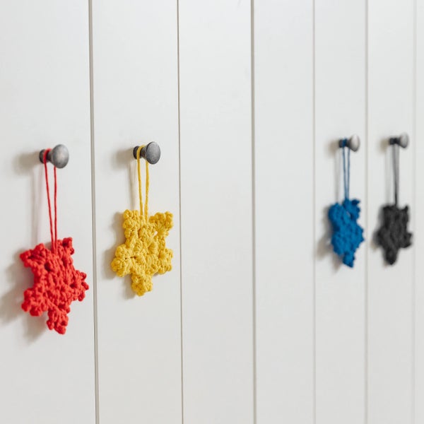 Rote, gelbe, blaue und schwarze gehäkelte Sternanhänger hängen an Möbelknöpfen aus Metall an einer vertäfelten Wand.