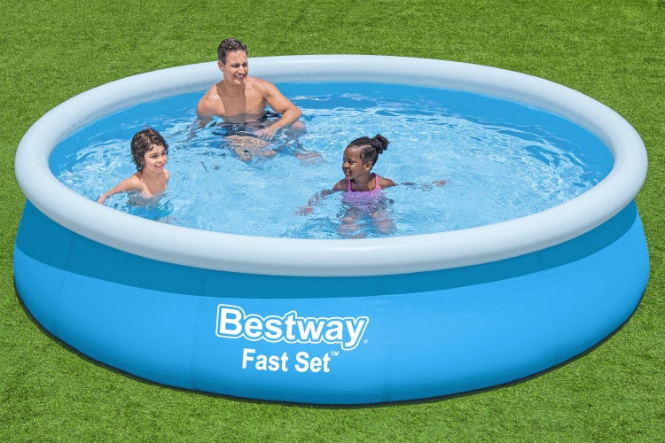 Runder blauer Bestway Fast Set Pool mit weißem Luftring auf einer Rasenfläche mit einem Mann und zwei Kindern im Wasser.