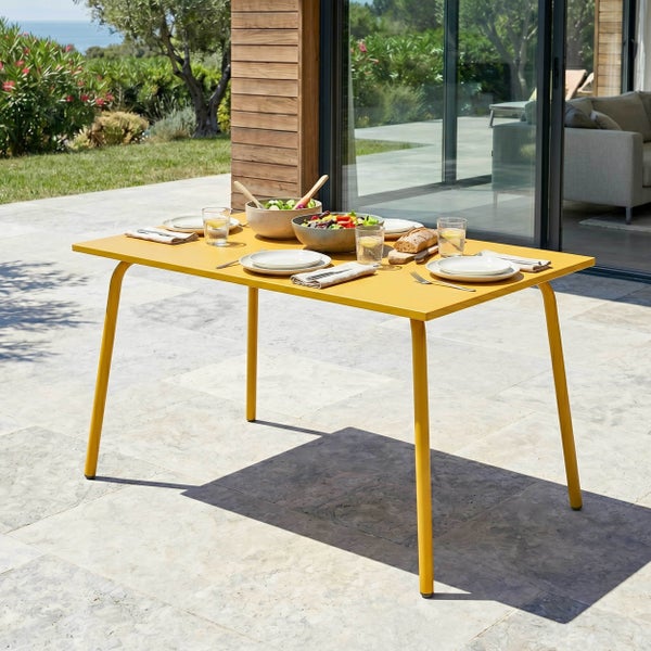 Gelber Gartentisch aus Metall, gedeckt mit Geschirr auf einer sonnigen, modernen Steinterrasse vor einem Haus.