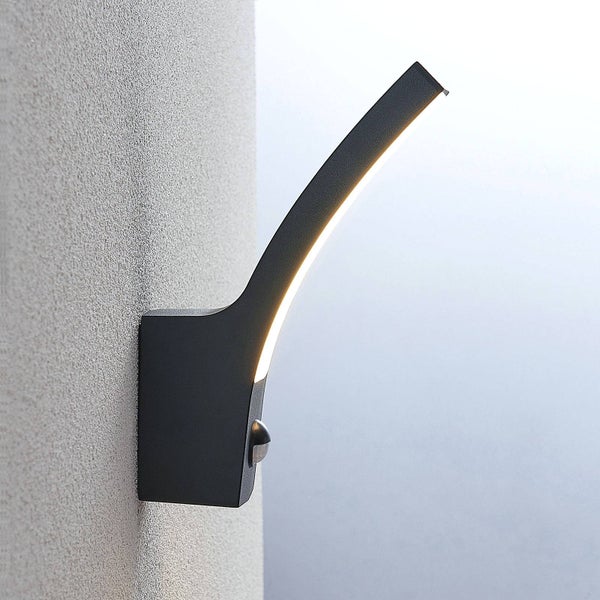 Moderne schwarze LED-Außenwandleuchte in gebogenem Design mit integriertem Bewegungsmelder, an einer strukturierten Wand montiert.