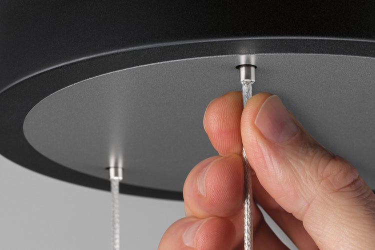 Hand justiert das Metallseil einer Pendelleuchte zur Höhenverstellung an der Deckenhalterung.