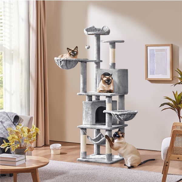 Katzenkratzbaum mit mehreren Ebenen, Höhlen und Liegeflächen mit drei Siamkatzen in einem Wohnzimmer.