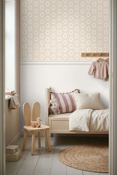 Ein Kinderzimmer mit gestreifter Mustertapete mit floralen Motiven, einer Holzbank, einem Hasenstuhl und einem runden Juteteppich.