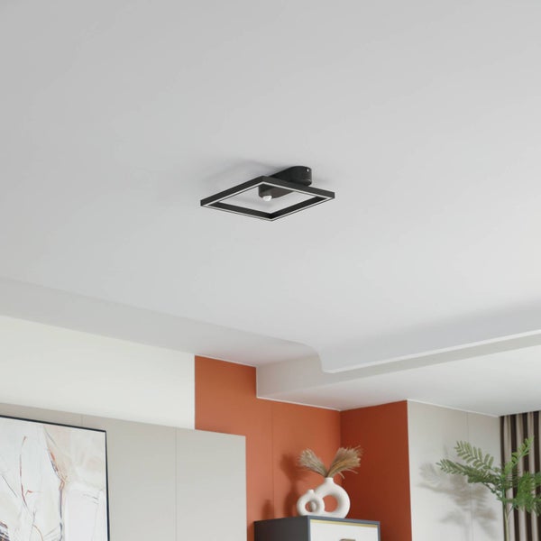 Moderne quadratische LED-Deckenleuchte in Schwarz an einer weißen Zimmerdecke in einem hellen Raum mit Inneneinrichtung.