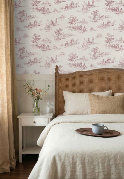 Helles Schlafzimmer mit Toile-de-Jouy-Tapete, weißer Wandvertäfelung, Bett mit Rattan-Kopfteil und weißem Nachttisch.