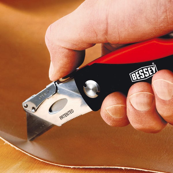 Bessey Logo. Hand schneidet mit einem Universalmesser ein Material.